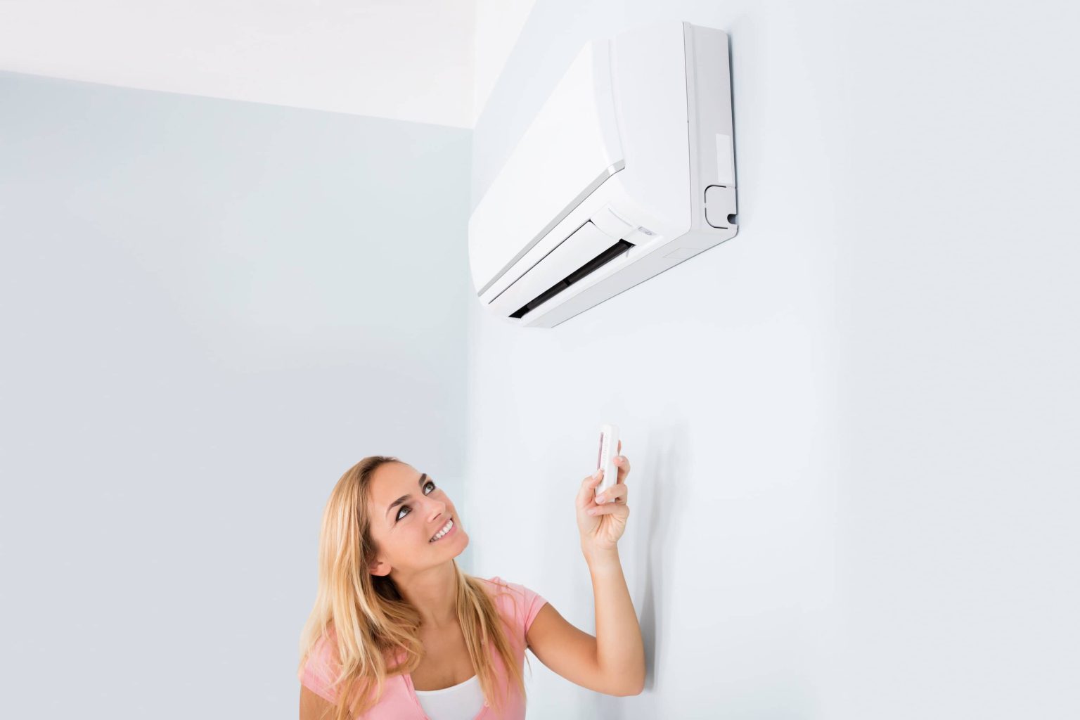 Portrait Of A Happy Woman Holding Remote Control In Front Of Air Conditioner At Home